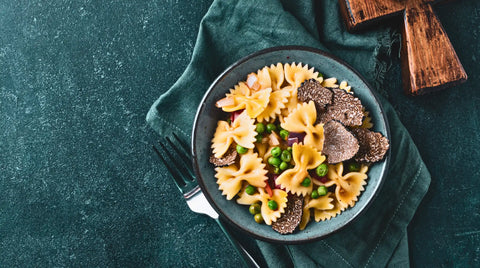Un bol de pâtes papillon avec des petits pois et des truffes noires tranchées