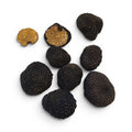 Sept truffes noires, dont deux moitiés laissant apparaître leur intérieur brun doré et rappelant une noix, disposées sur un fond blanc uni.