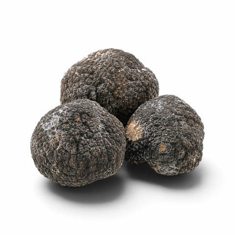 Trois truffes entières congelées, légèrement couvertes de givre naturel, sur fond blanc